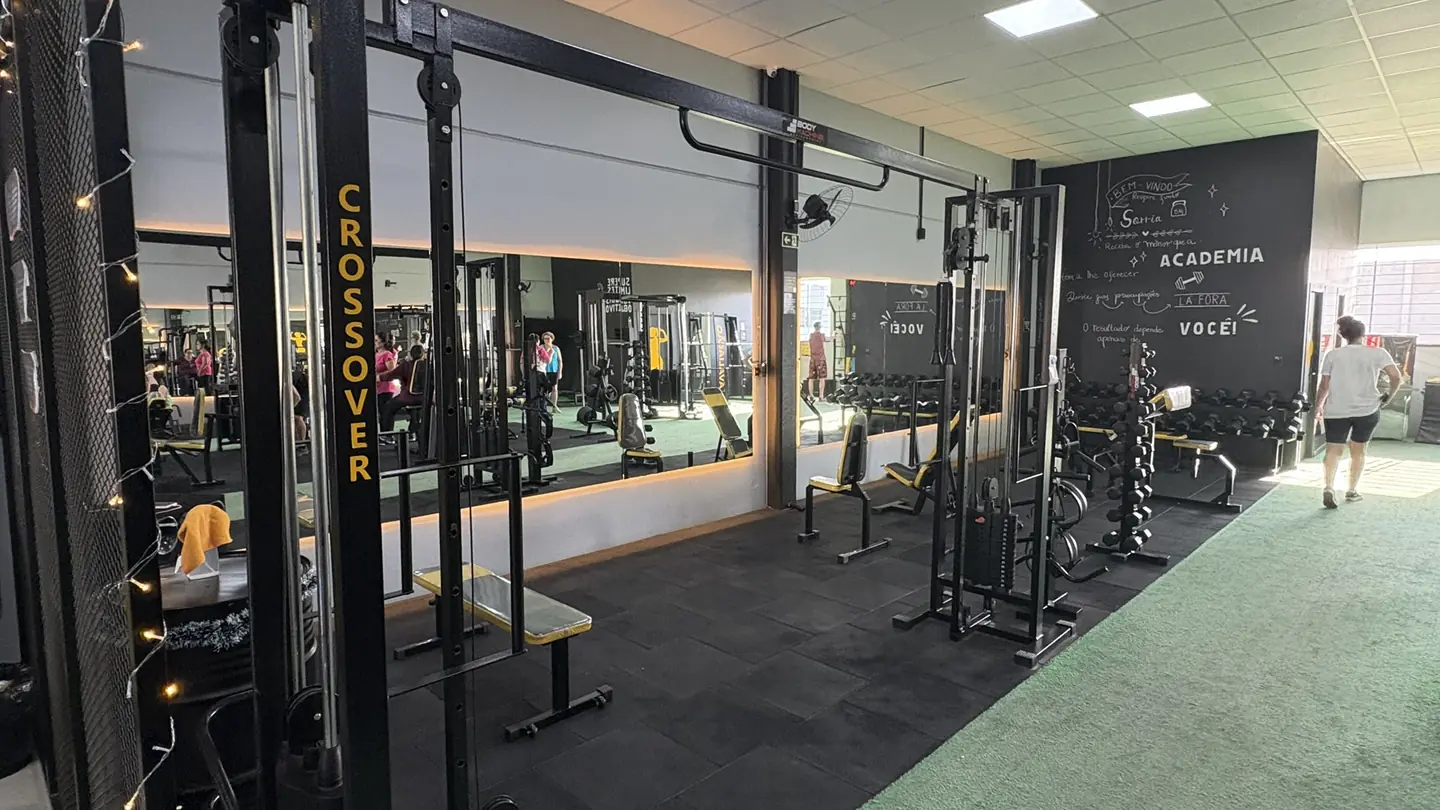 Salão da Superação Gym com estação de crossover, halteres, espelhos e piso emborrachado.