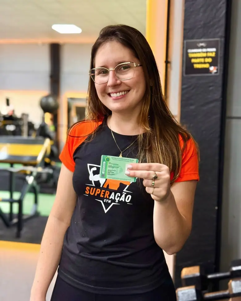 Júlia Brandão, responsável técnica da Superação Gym, segurando a carteira profissional do CREF.