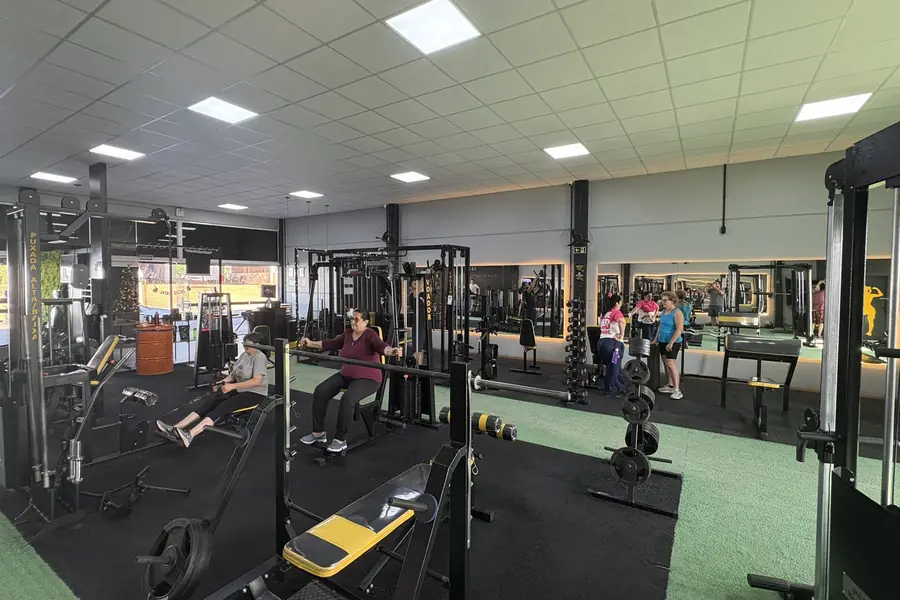 Racks de agachamento, barras e bancos na área de musculação da Superação Gym.